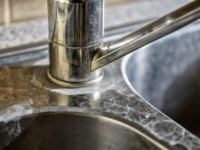 Close-up of a kitchen tap and sink with hard water calcification.