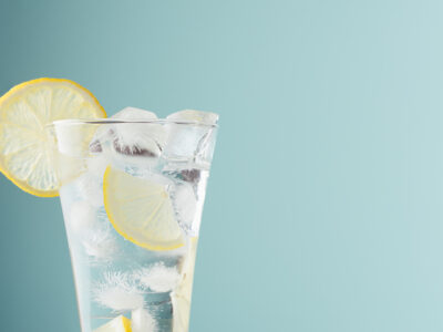 Healthy fresh tonic with lemon, ice cubes, soda in misted glass on pastel green color background, closeup, half, details, top.
