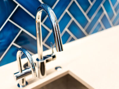 New modern faucet and kitchen sink closeup with countertop, blue vibrant backsplash and shiny clean stainless steel handle